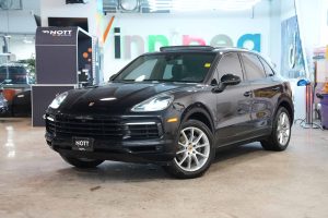 A black 2020 Porsche Cayenne displayed in the Nott Autocorp Winnipeg showroom. The wheels are turned to show the Porsche badges clearly.