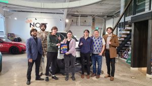 A group of people who work at Nott Autocorp standing in front of a Rivian R1T, a fully electric truck. They are holding a first place plaque from World of Wheels 2026.
