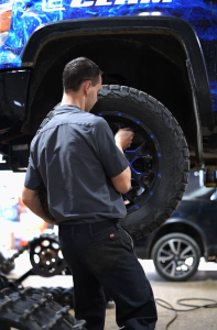 An automotive technician changing the tire on a blue truck.